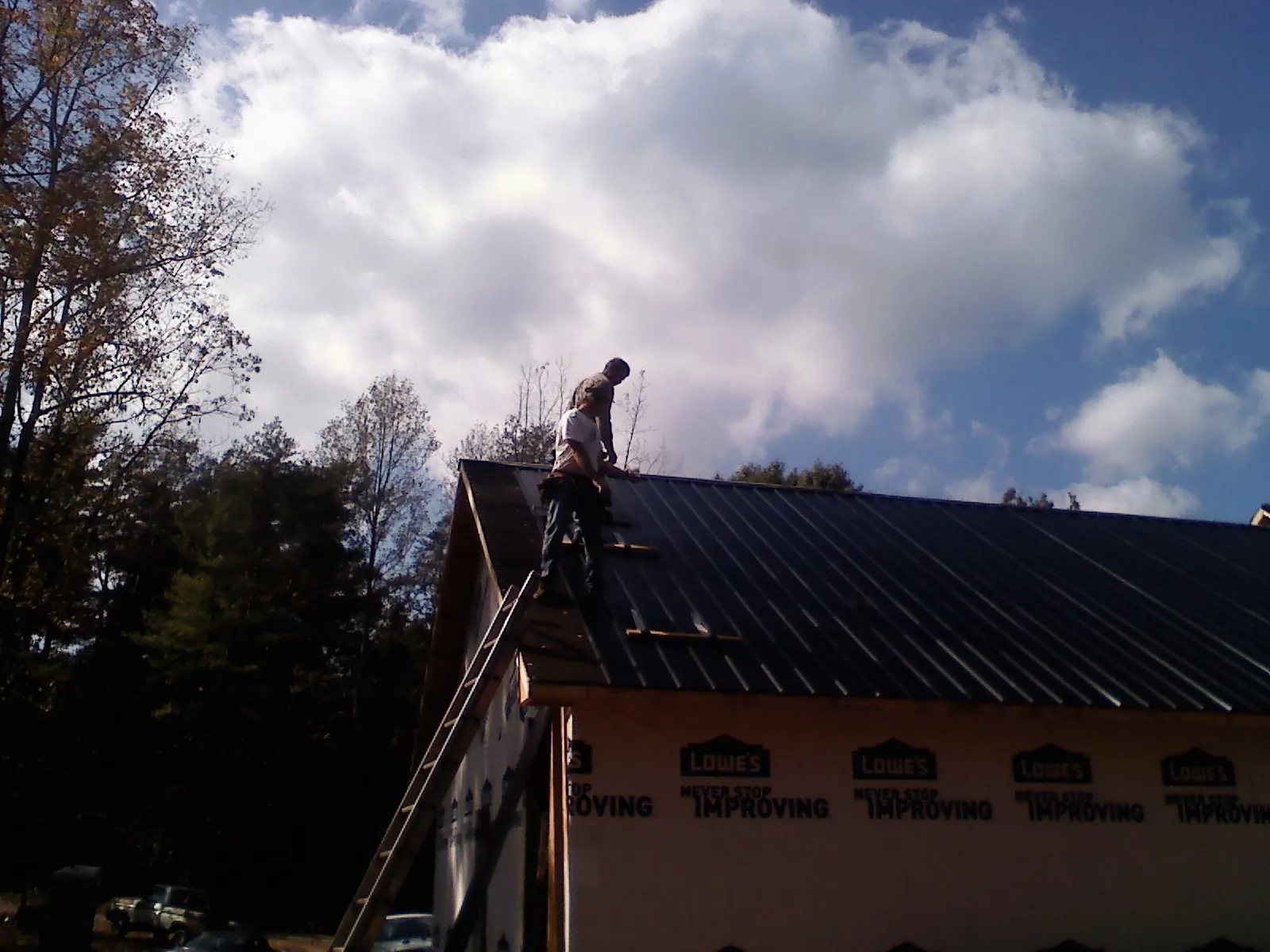 Roofer fastening dark metal panels high against a cloudy sky, from a Roof Inspection job in Akron